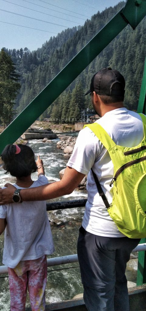 Father and daughter looking at the Uhl River from a bridge in Barot Valley @traxplorers
