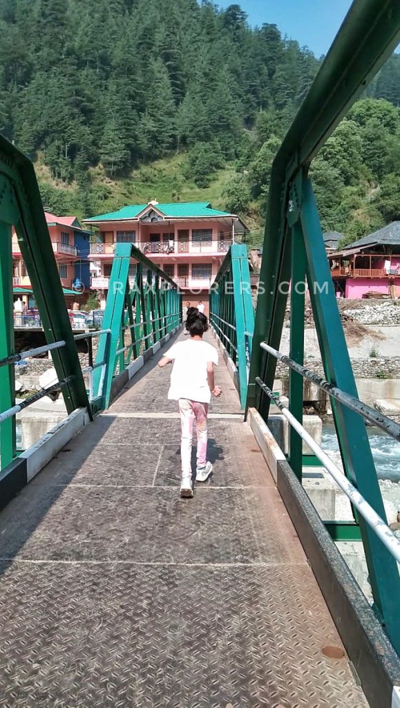 walking across a green iron bridge in Barot village, Himachal Pradesh