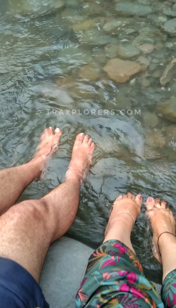 Family soaking feet in the cold water of the Uhl River, Barot Valley